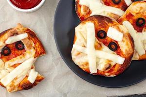 Mini pizza as mummy for kids with cheese, olives and ketchup. Funny crazy Halloween food for children. photo