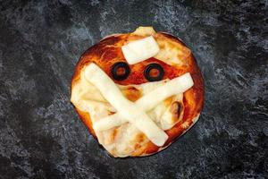 Mini pizza as mummy for kids with cheese, olives and ketchup. Funny crazy Halloween food for children. photo
