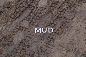 la palabra barro colocada con letras de metal plateado en la superficie de tierra mojada foto