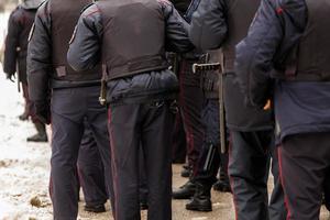 Tula, Russia  January 23, 2021 Crowd of police officers in black uniform with bulletproof vests and pistols - view from back. photo