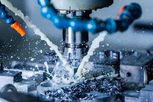 a process of vertical cnc steel milling with external water coolant streams, splashes and a lot of metal chips - close-up with selective focus photo