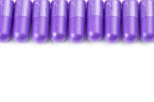 row of proton purple color organic capsules isolated on white background closeup with selective focus photo