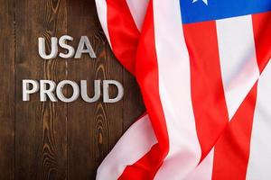 words USA proud laid with silver metal letters on brown wooden surface with flag of United States of America photo