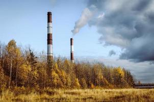 Red and white chimneys of the power plant exude smoke that mixes with low dark clouds photo