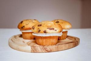 tres deliciosos muffins con trozos de chocolate en una bandeja de madera sobre una mesa blanca foto