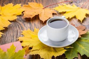 taza de café sobre una mesa de madera con un libro y coloridas hojas de arce otoñales foto