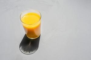 a glass of orange juice on a gray concrete background in bright sunlight photo