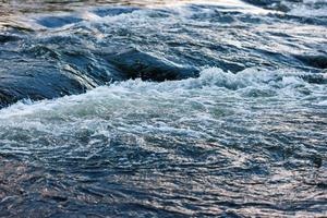 agua que fluye de un río de verano con una pequeña cascada rápida a la luz del atardecer foto