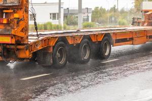 Remolque de cubierta escalonada naranja de doce ruedas que se mueve en una carretera mojada en un día lluvioso con salpicaduras de agua foto