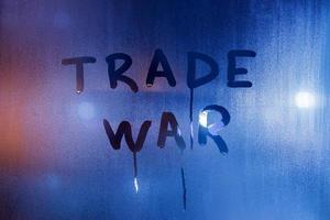 the phrase trade war handwritten on classic blue night wet window glass photo