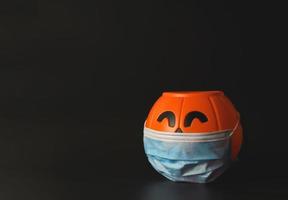 calabaza de halloween de plástico con mascarilla médica sobre fondo negro con espacio para copiar. nuevo concepto normal de halloween foto