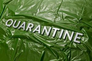 the word quarantine laid with silver letters on green crumpled plastic film background in diagonal perspective photo