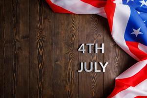 the words 4th july and crumpled usa flag on flat textured wooden surface background photo