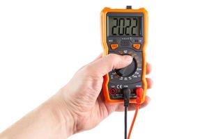 digit 2022 on lcd screen of digital electrical multimeter in left hand, isolated on white background photo