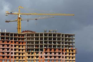 building process of large residential apartment building with crane on cloudy sky background photo