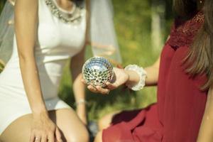 Girls in summer in dresses sit on grass. Girl holds ball in her hand. Mirror ball in palm of your hand. photo