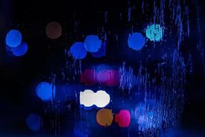 an abstract background of red and blue police lights bokeh trough wet glass at night close-up with selective focus photo