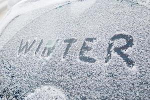 word winter handwritten on snowy car window at winter morning light photo