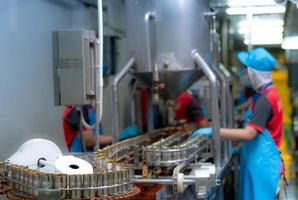 Canned fish factory. Food industry.  Sardines in red tomato sauce in tinned cans on conveyor belt at food factory. Blur workers working in food processing production line. Food manufacturing industry. photo