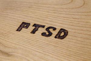 an abbreviation PTSD - post traumatic stress disorder - burned by hand on flat wooden board in diagonal composition photo