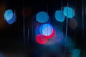 an abstract background night blue and red street lights bokeh through wet glass, close-up with selective focus photo