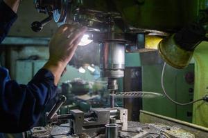 Industrial steel drilling process with smoke. Close-up with selective focus. Manual feed by hand. Workpiece in vise on table. photo