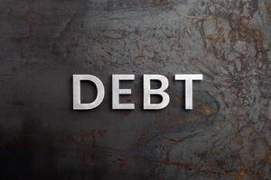 the word debt laid with silver letters on raw rusted steel sheet surface in flat lay perspective photo