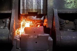 close-up frontal view of hot steel forging process with big mechanical hammer machine photo