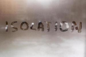 the word isolation handwritten on wet window glass at cloudy weather - close-up with selective focus and background blur photo