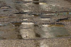 baches y charcos en la mala carretera de asfalto húmedo roto después de la lluvia foto