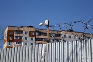 residential multi-storey building behind a fence with barbed wire and small surveillance camera photo