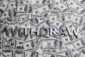 The word WITHDRAW laid with aluminium letters on the US dollar banknotes background - with selective focus photo