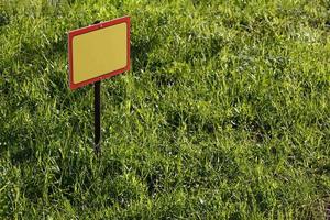 blank yellow sign mockup on green lawn background - close-up with selective focus photo