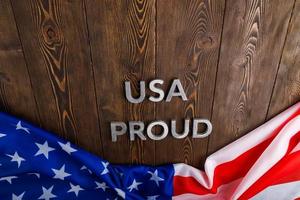 words USA proud laid with silver metal letters on brown wooden surface with flag of United States of America photo