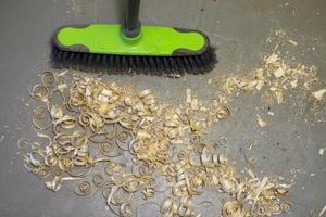 a small pile of wood shavings on a gray linoleum floor with a broom brush photo