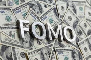 The word FOMO laid with aluminium letters on the US dollar banknotes background - with selective focus photo