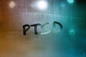 an abbreviation PTSD - post traumatic stress disorder - handwritten on wet glass of night window photo