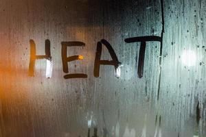the word heat written on night wet window glass close-up with bokeh background photo
