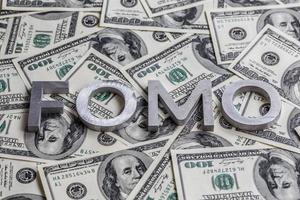 The word FOMO laid with aluminium letters on the US dollar banknotes background - with selective focus photo