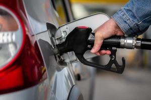 hand in jeans jacket refueling gray metallic car on gas station - closeup photo