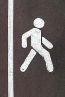 Señal de calle blanca para caminar en la carretera asfaltada de la ciudad gris con franja vertical foto