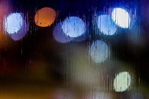 un fondo abstracto luces de la calle de noche bokeh a través de vidrio húmedo, primer plano con enfoque selectivo foto