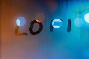 the word lofi written by finger on night wet window glass, blue and orange colors photo