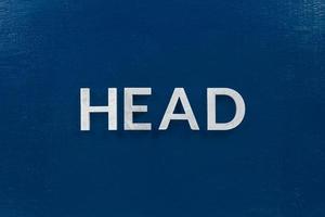 the word head laid with silver metal letters on classic blue painted board background photo