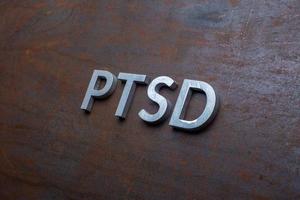 the word PTSD laid with silver metal letters on flat rusted steel sheet background in slanted diagonal perspective photo