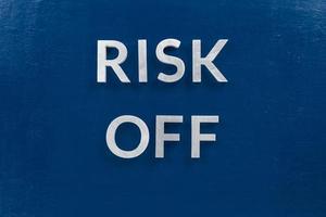 the words risk off laid with silver metal letters on classic blue surface for stock market background photo