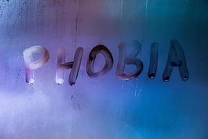 the word phobia handwritten on wet foggy window glass surface with blue background light photo