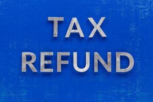 the words tax refund layed on blue painted board with thick silver metal aphabet characters photo
