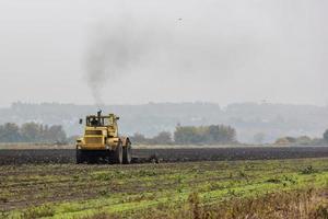 grim yellow tractor plows the field after harvest before winter at cloudy and foggy autumn morning photo