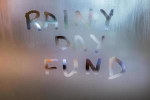 words RAINY DAY FUND written by hand on wet glass at morning with blurry street light background photo